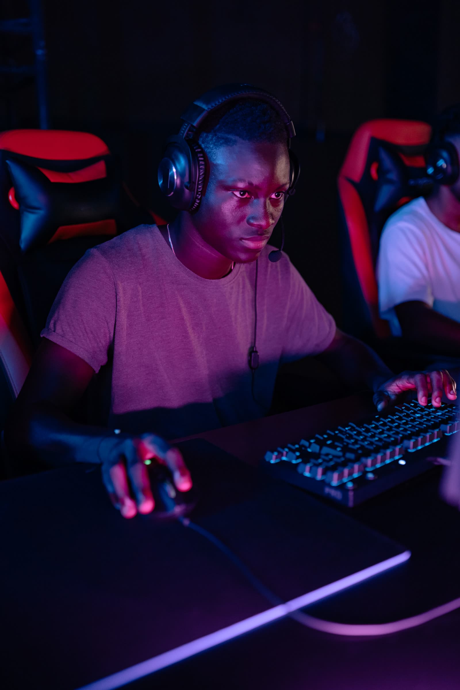 A focused player in a headset with mic gripping mouse and mechanical keyboard under purple light
